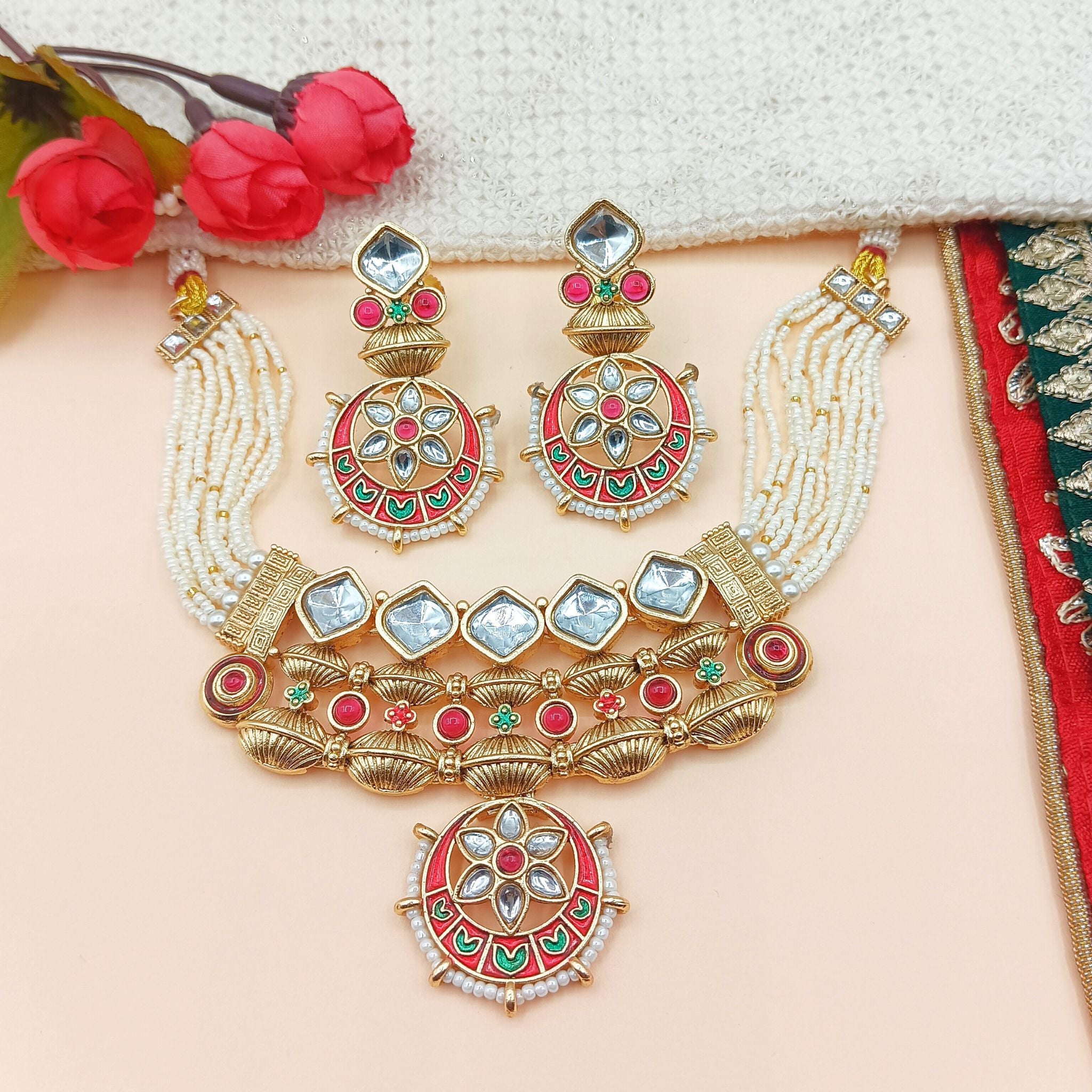 Ornate necklace and earrings set with red and gold colors on a beige background