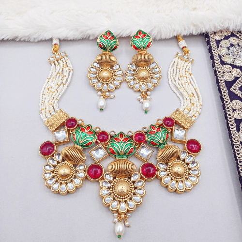 Ornate necklace and earrings with gold, red, and green colors on a white background.