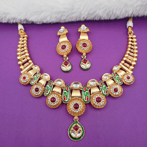 Gold necklace and earrings with red and green accents on a purple background