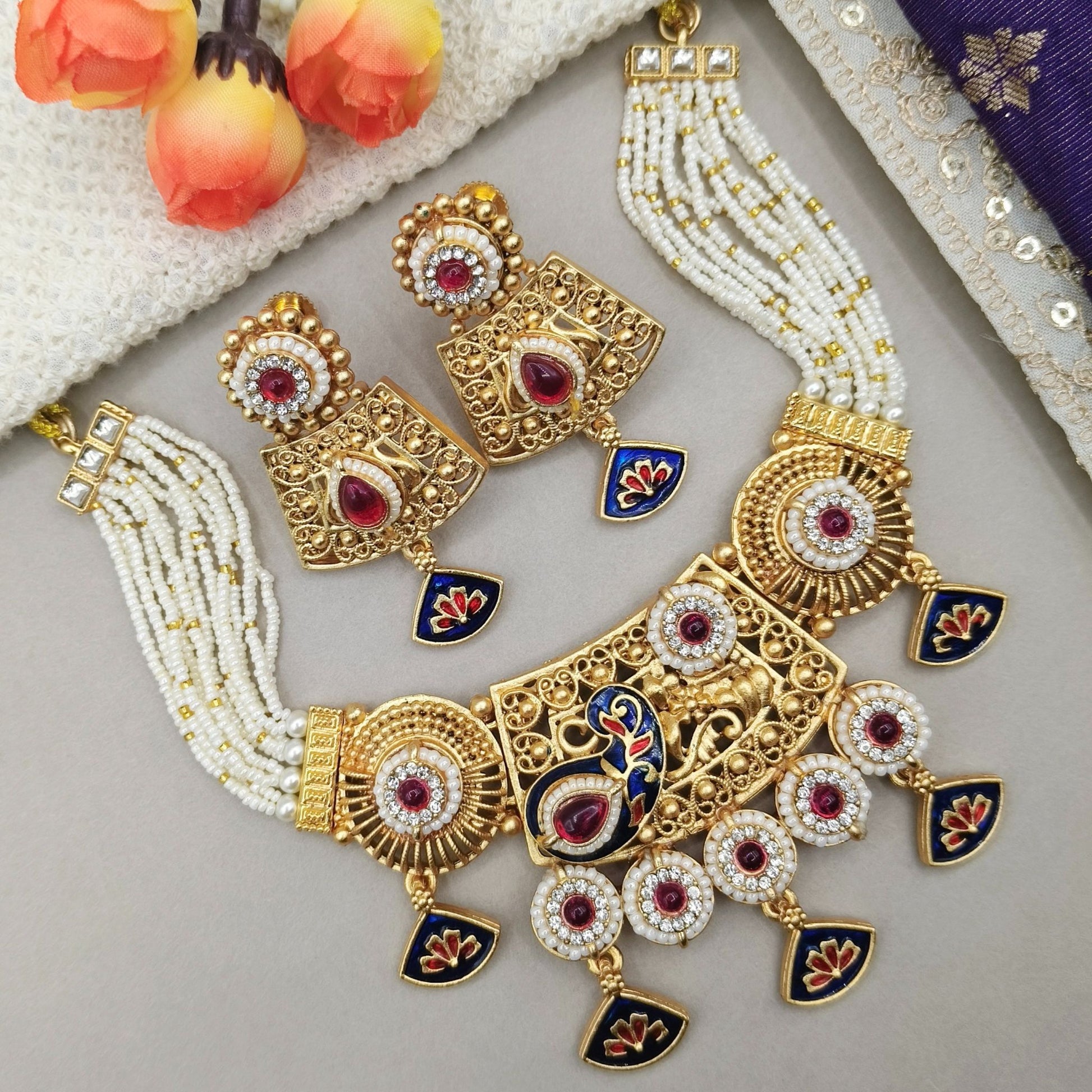 Ornate gold and pearl necklace with red gemstones on a light gray surface.