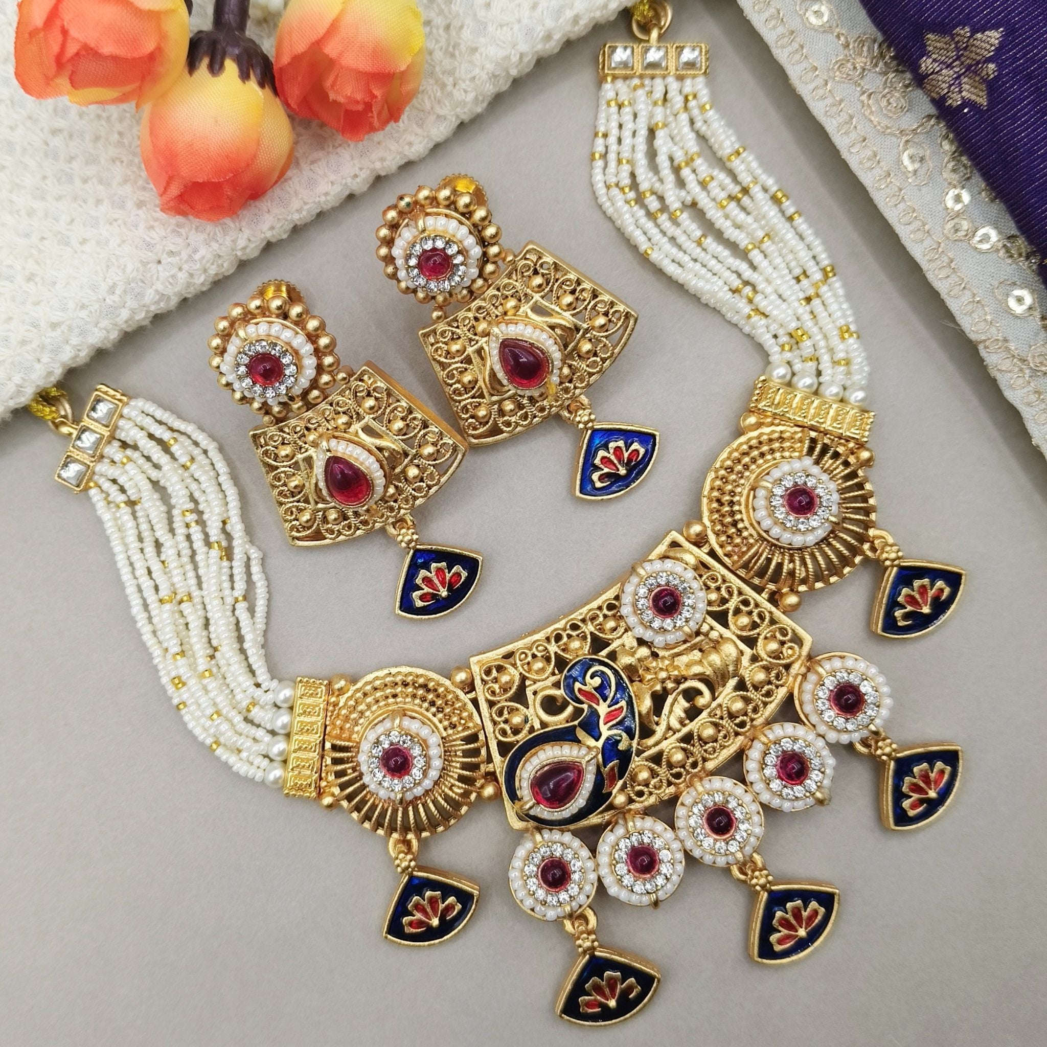 Ornate gold and pearl necklace with red gemstones on a light gray surface.
