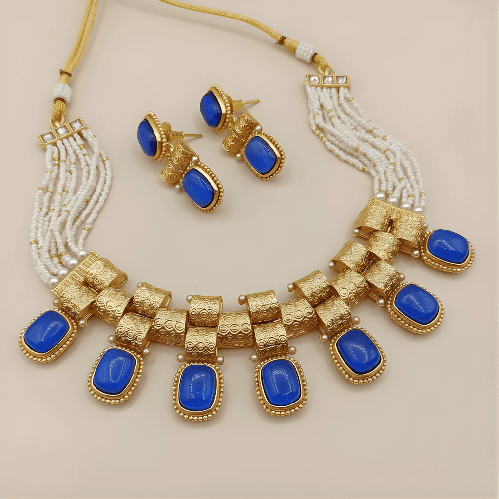 Gold necklace with blue stones and matching earrings on a beige background