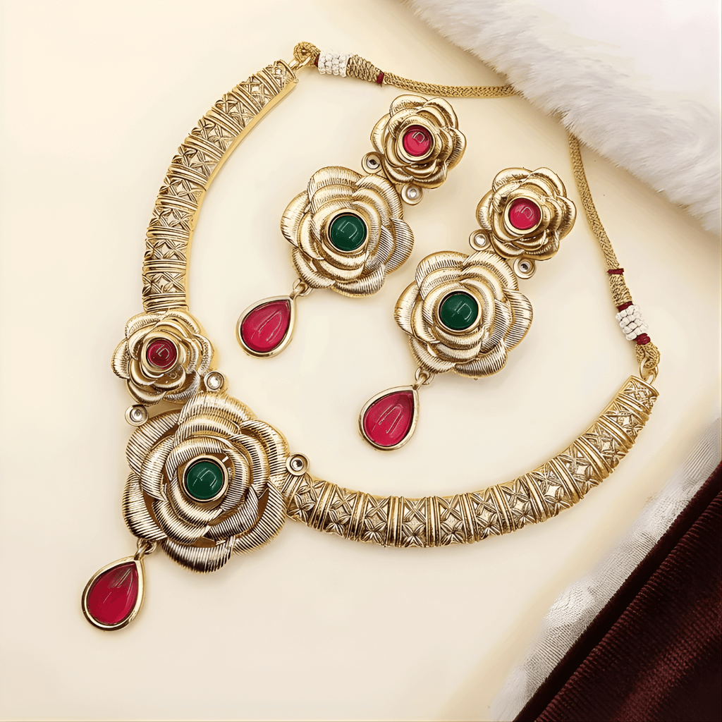 Gold necklace with floral designs and red and green gemstones on a white surface