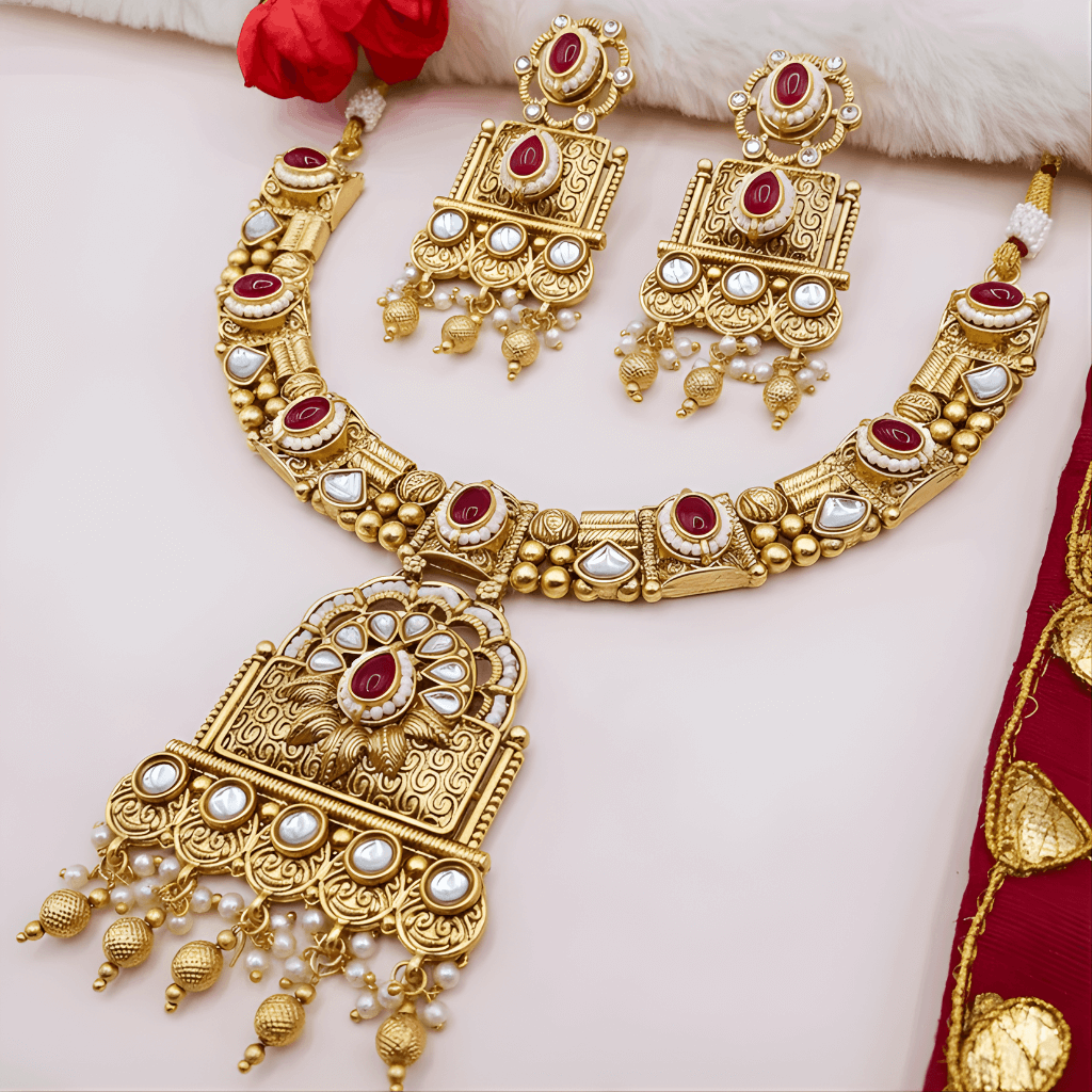 Gold necklace and earrings set with red and white stones on a light background