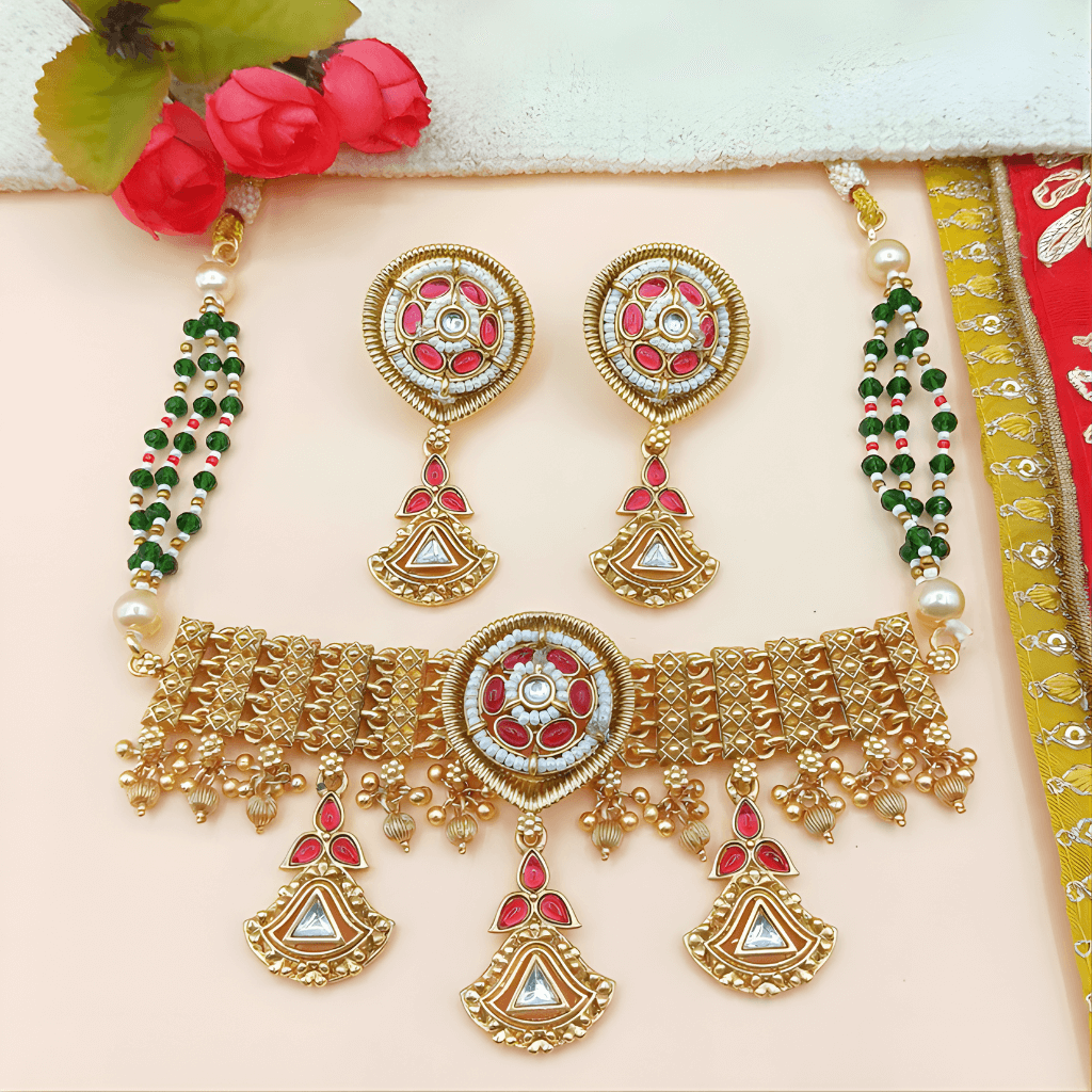 Gold jewelry set with red and green accents on a light pink background