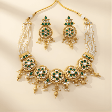 Gold necklace with green gemstones and pearl accents on a beige background