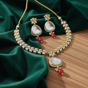 Gold necklace with white stones and red beads on a green fabric background