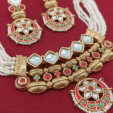 Ornate gold necklace with red, green, and white stones on a red background