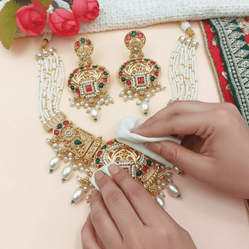 Ornate gold and gemstone jewelry set with a hand cleaning it using a cloth.