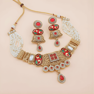 Ornate gold necklace with red and green accents on a beige background