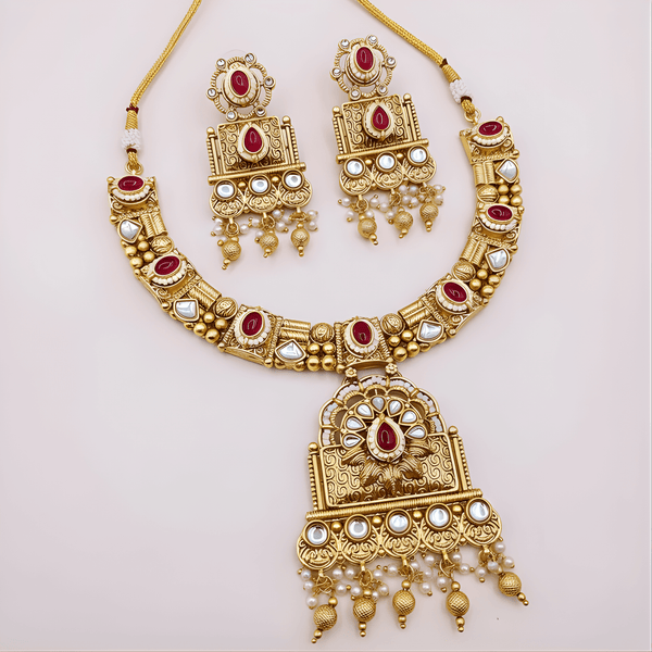 Gold necklace and earrings set with red and white stones on a light pink background
