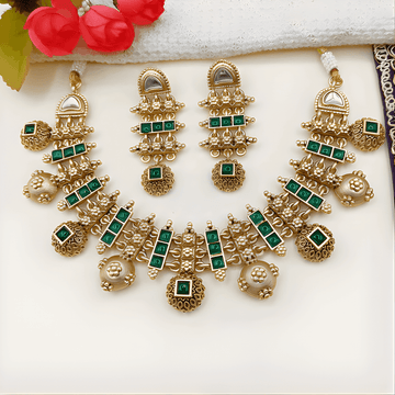 Gold and green gemstone jewelry set on a white surface with red flowers in the background