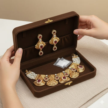 Gold jewelry set with red gemstones in a brown jewelry box held by hands.
